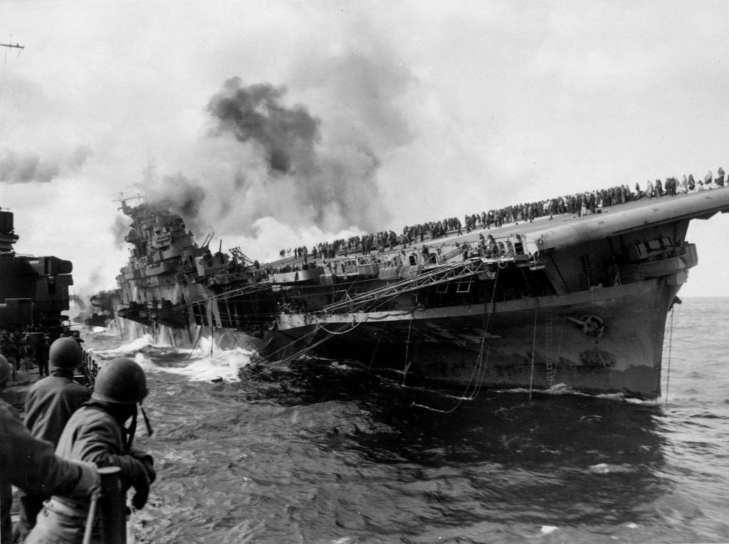 Porte-avions en feu symbolisant les destructions humaines et les conséquences des guerres sur la planète Terre