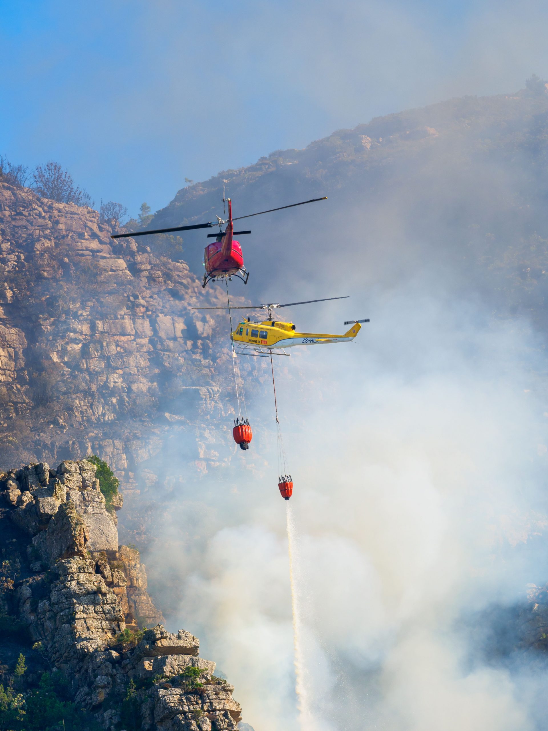 Deux hélicoptères larguent de l’eau sur un violent incendie de forêt dans une région montagneuse