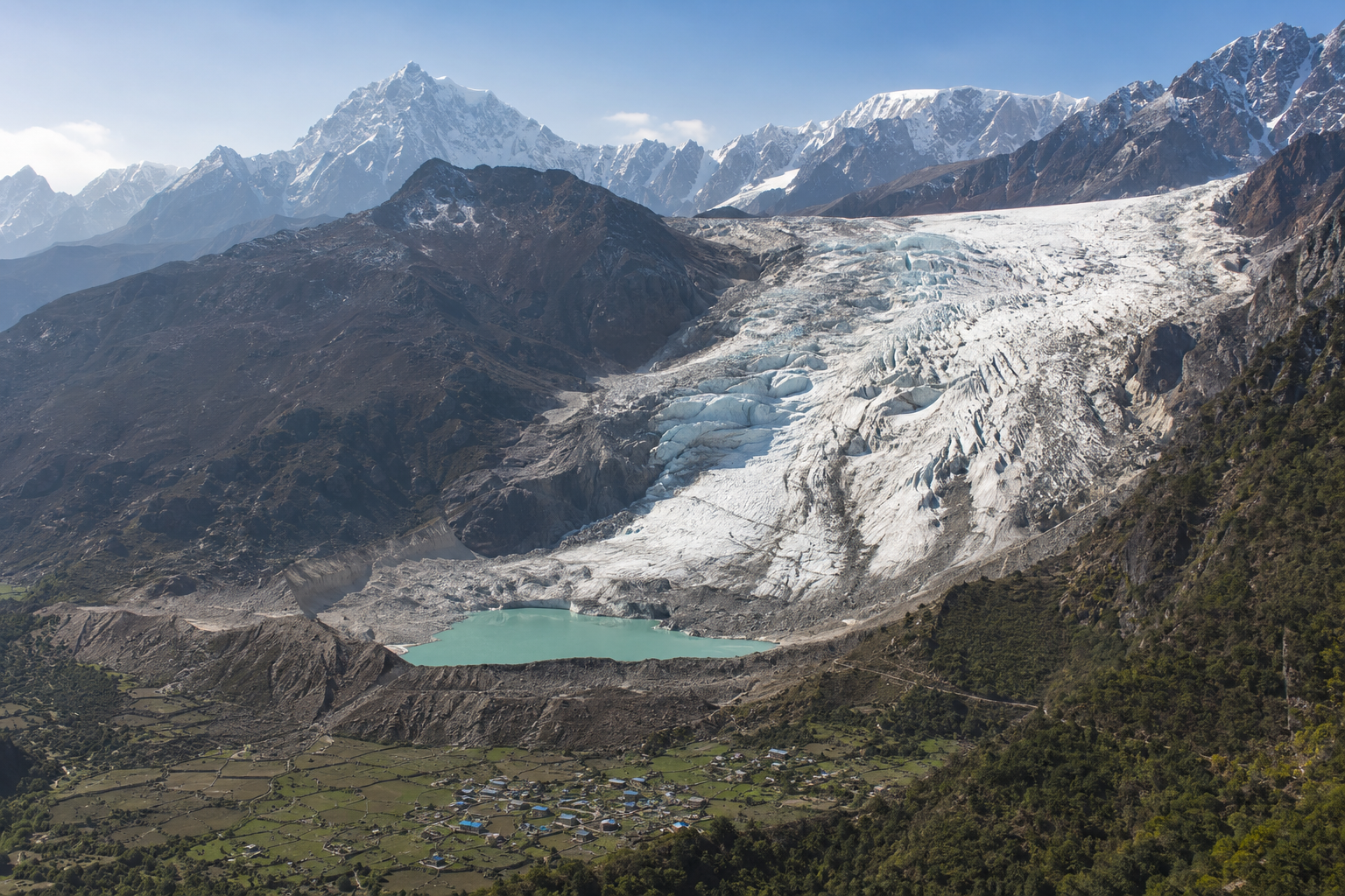 Glacier fissuré et lac glaciaire dominant une vallée habitée de l’Himalaya